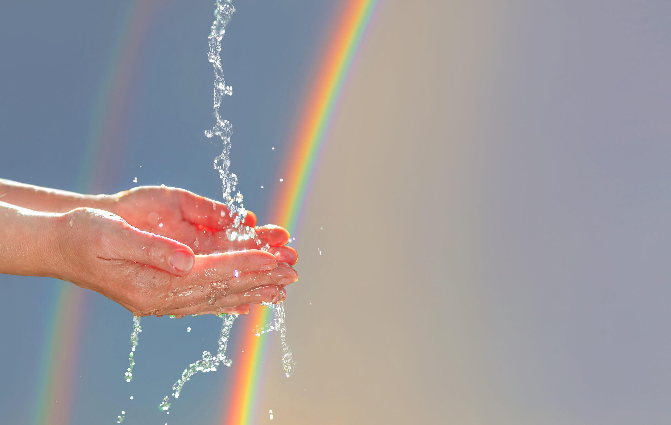 Water pours into women's hands and palms on a rainbow background for eco design